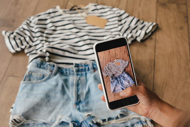 A hand holding a phone and taking a photo of clothes to sell on Vinted