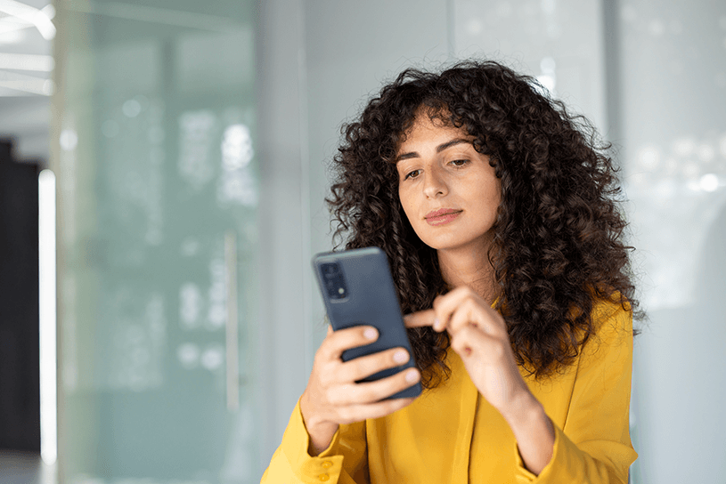 Woman in yellow shirt looks at mobile phone in a concerned way