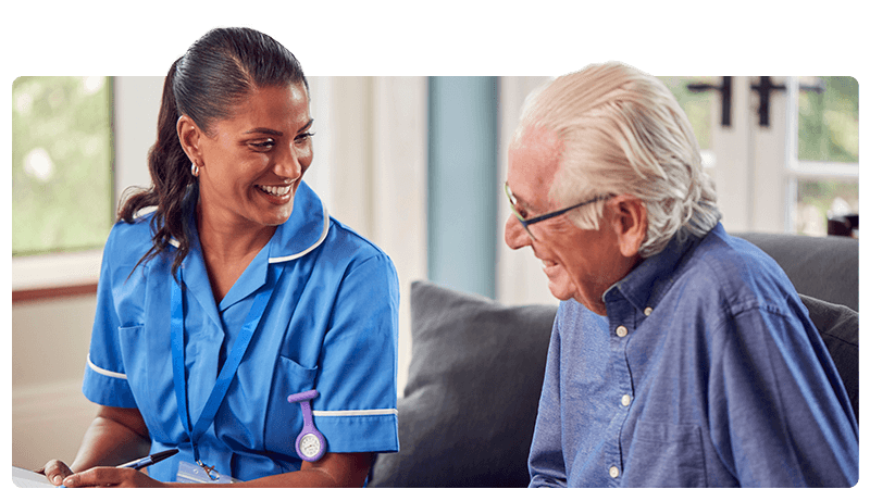 A carer in a blue uniform talking to an elderly man